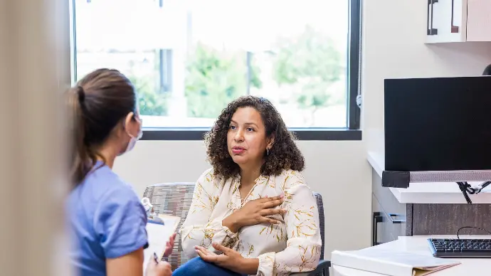 Nurse talking to a patient in an urgent care clinic, the patient is pointing to the area of their chest near their left shoulder.