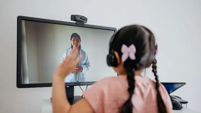 A young girl waves at a doctor displayed on screen.